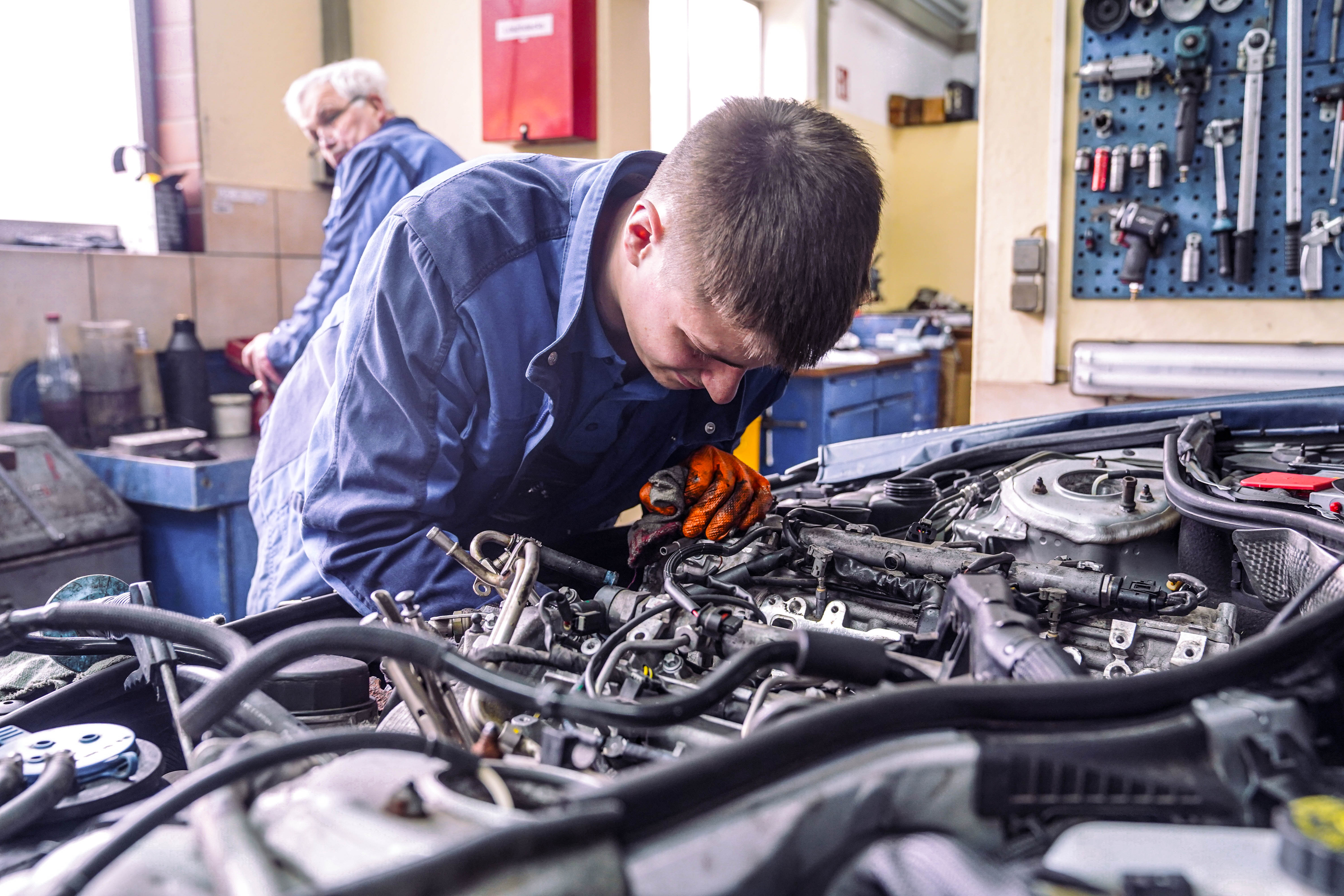 Junger Mechatroniker arbeitet konzentriert am Motor, Senior im Hintergrund